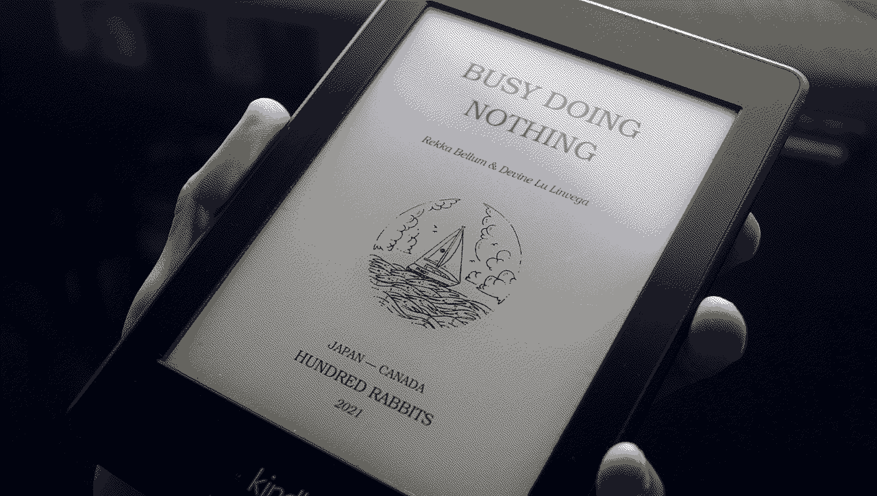 A hand holding a Kindle featuring the cover of our book Busy Doing Nothing