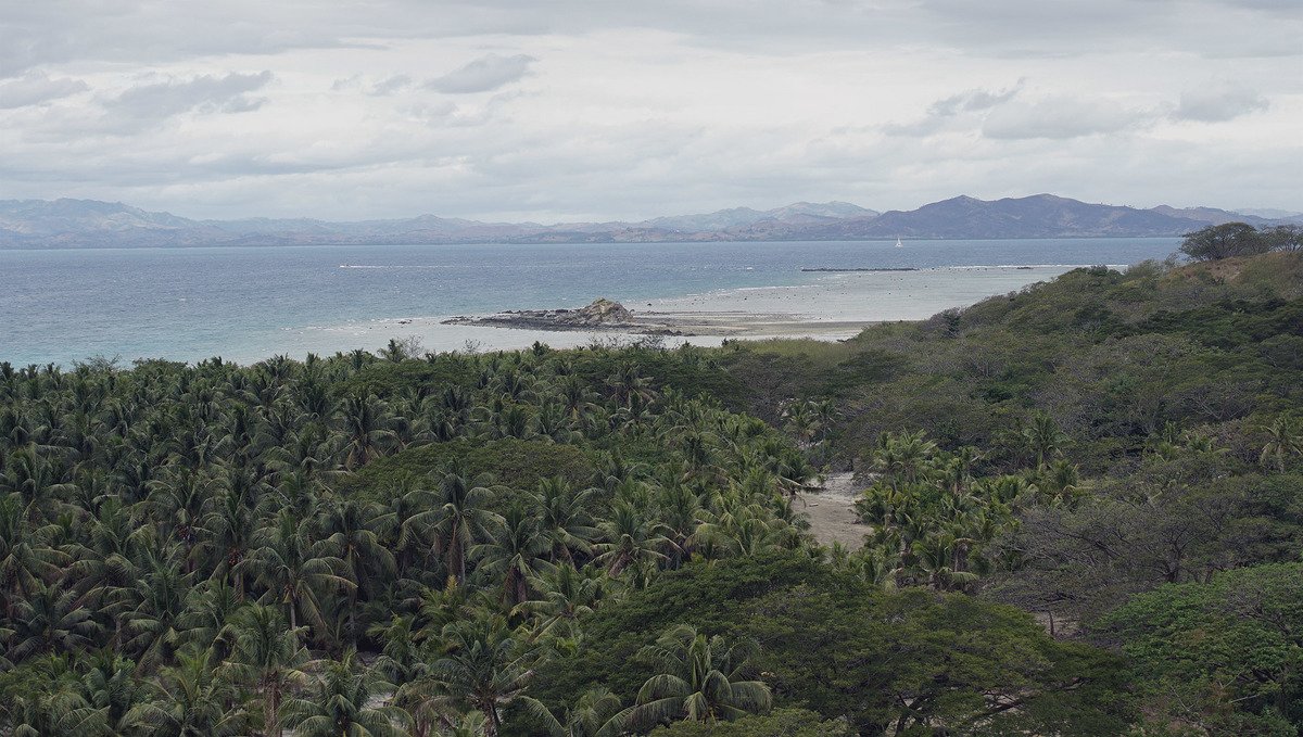 A view of mainland Fiji from an island, surrounded by reefs and tropical trees