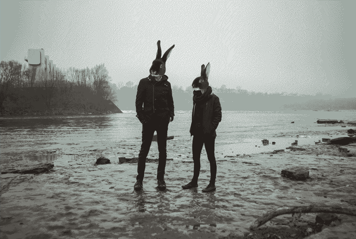 A dithered photo of two people with rabbit heads standing near a river