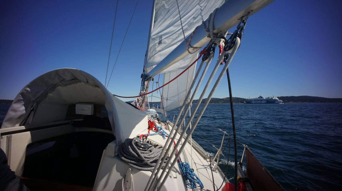 view from the deck of a sailboat, at sail, with a ferry crossing the bow of the vessel