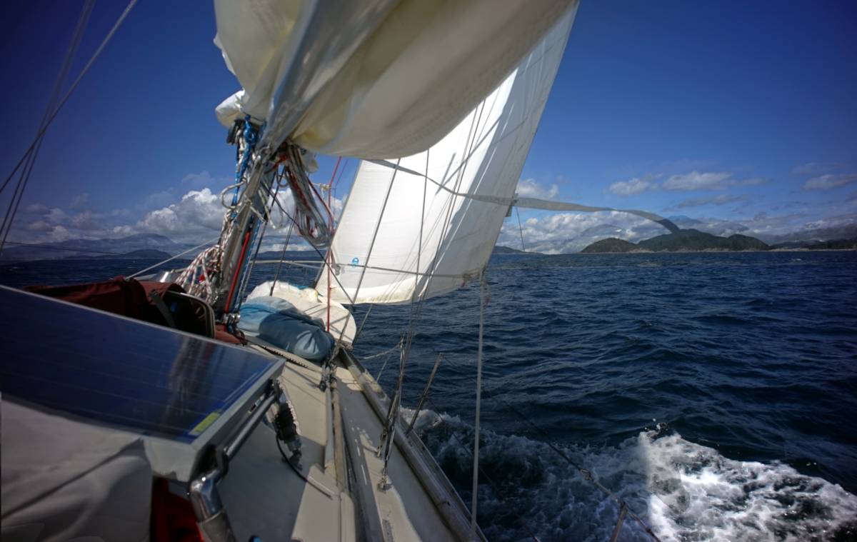 a sailboat at sail, heeling, with a view of some islands ahead on a clear, sunny spring day