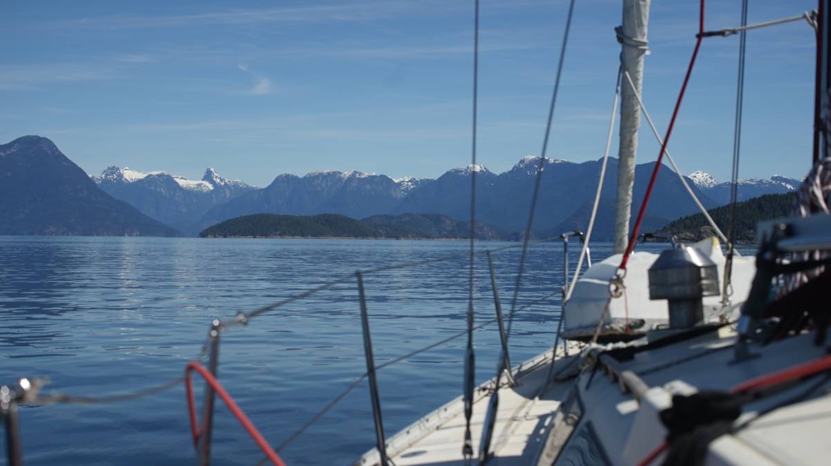 a shot taken from the cockpit of a sailboat showing calm waters and beautiful snowcapped mountains ahead