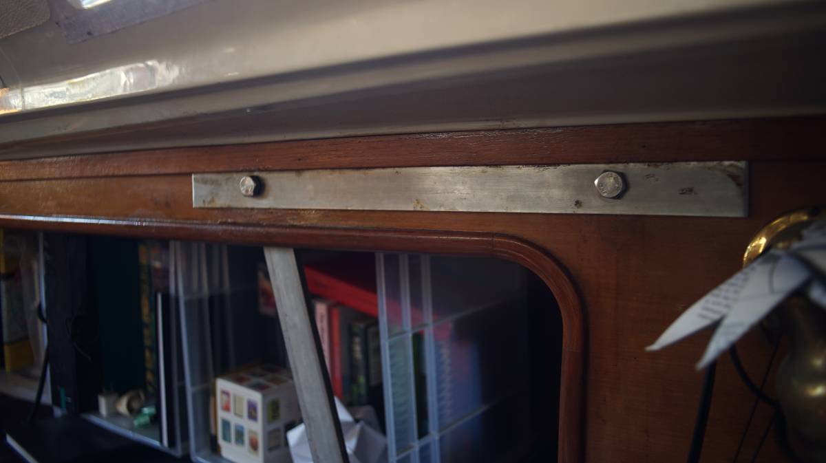 a length of metal linking the two upper bolt holes of two separate chainplates, and keeping them fixed to a wall inside a sailboat cabin.