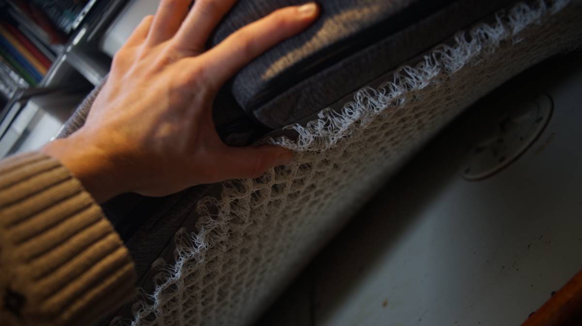 a hand lifting a cushion to show the mesh lining