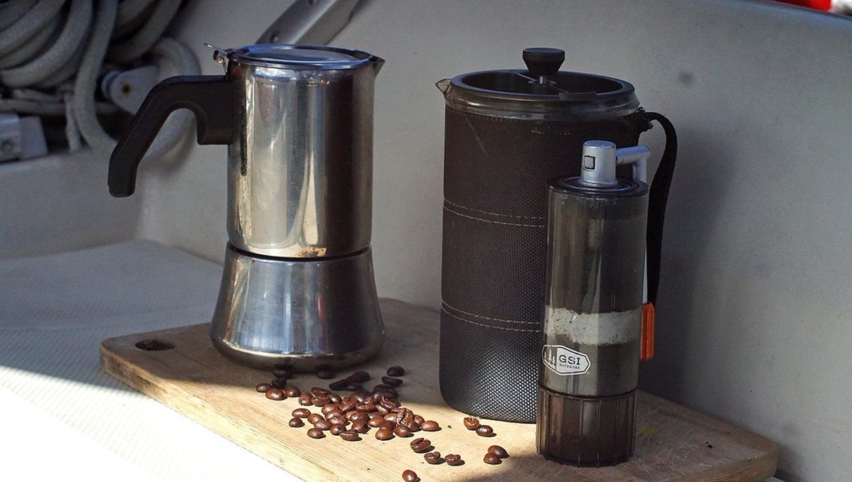 A photo of a mokapot, a french press and a coffee grinder, outside