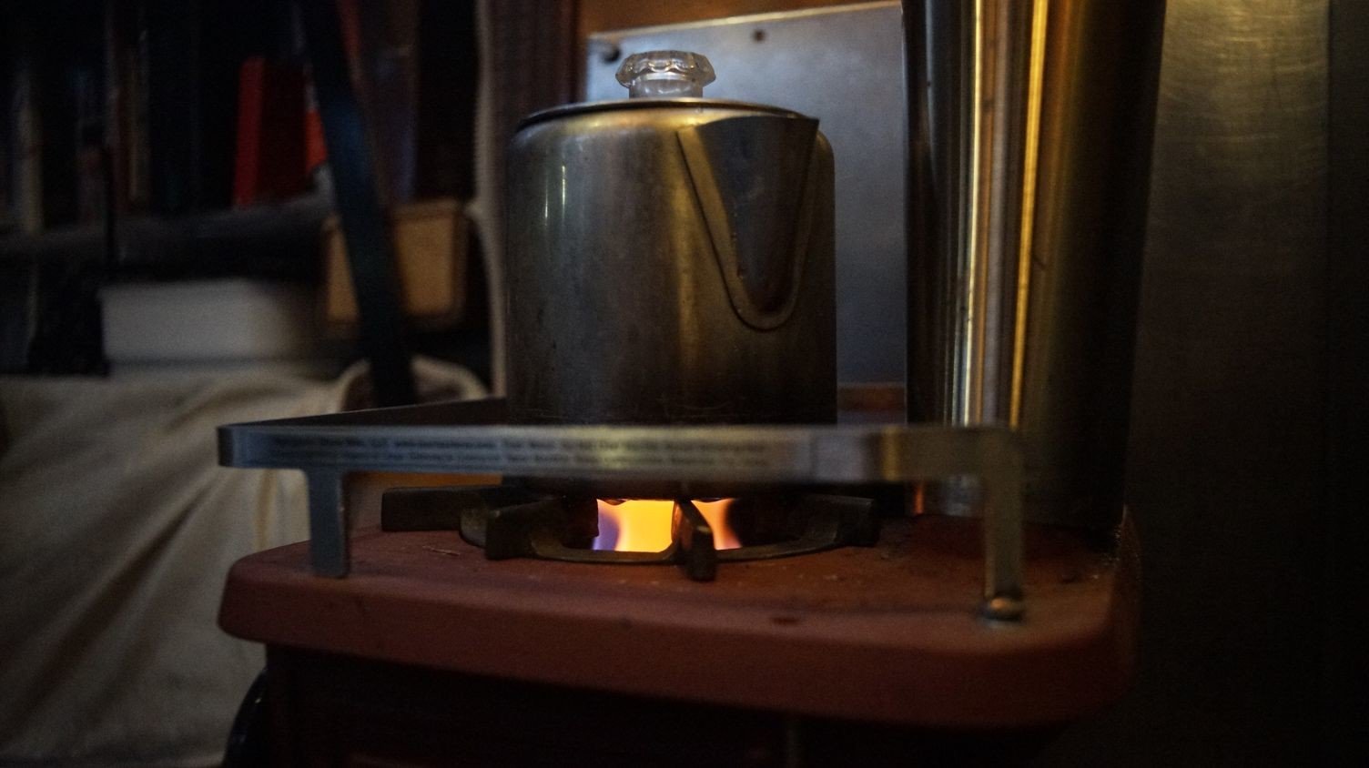 A photo of an alcohol burner nestled in a woodstove heating a kettle of water