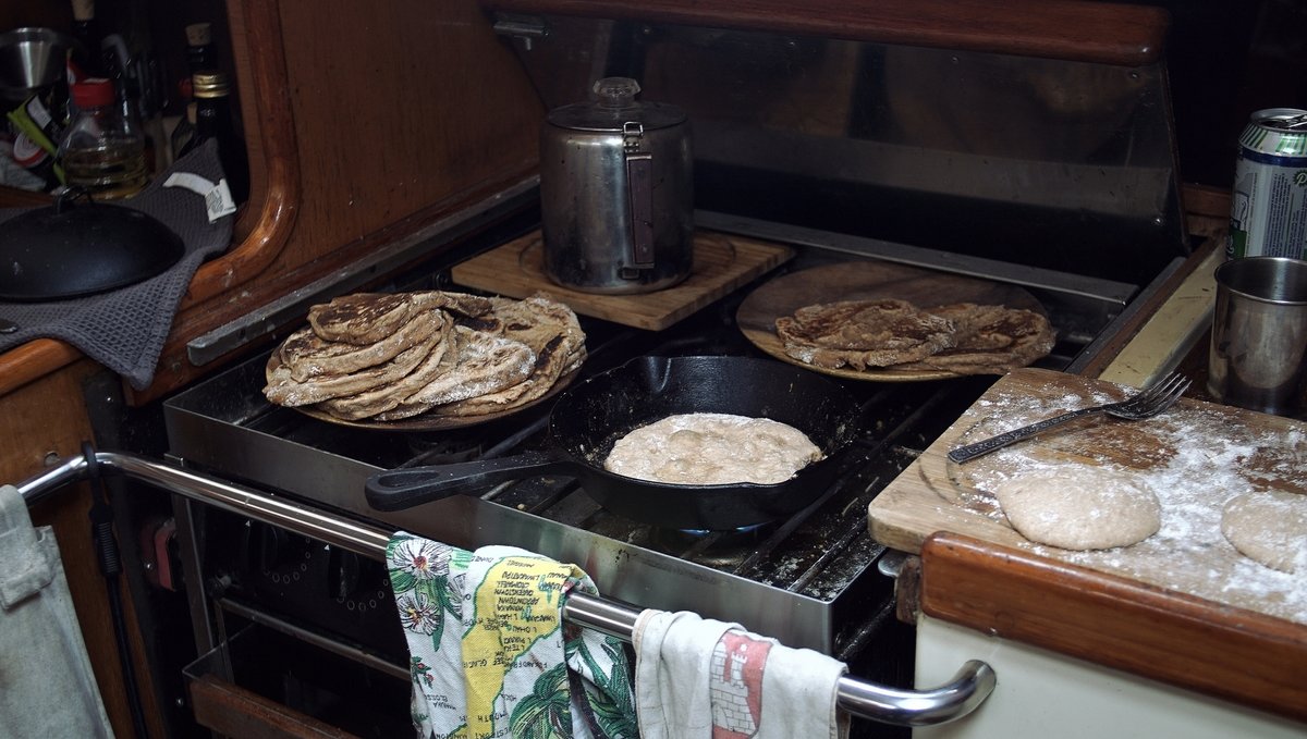 The photo of a sailboat galley with a gas cooking range, a pita is cooking in a cast iron pan