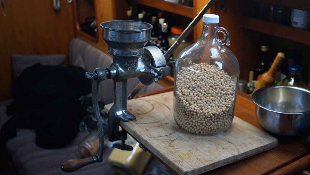 A photo of a grain mill next to a glass carboy of whole dry soybeans