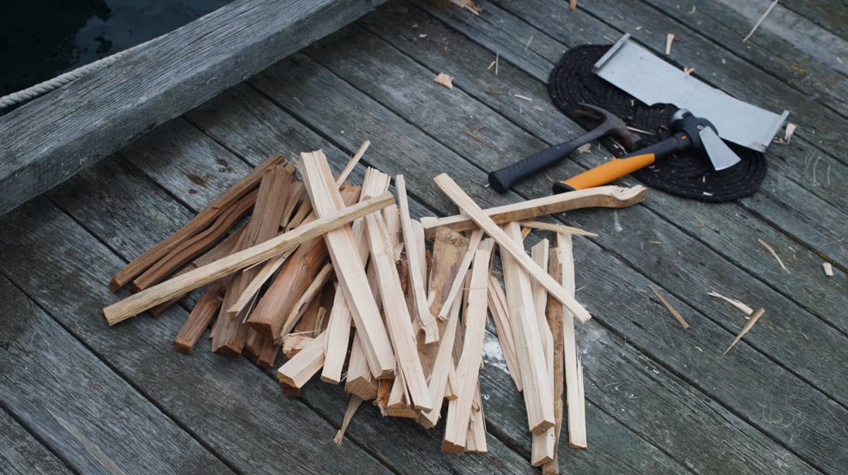 some kindling laying in a pile on the dock next to woven rope mat, a hatchet and a hammer