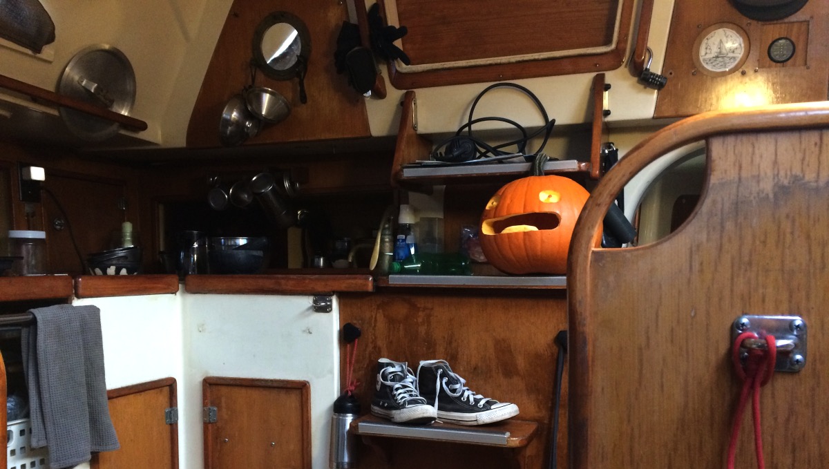 the calcifer pumpkin is on the stairs in the companionway of a sailboat, grinning, having a grand ol time