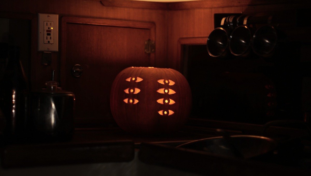 A photo of a candle-lit carved pumpkin with 3 eyes aligned vertically with 4 eyes next to those for an assymetric look