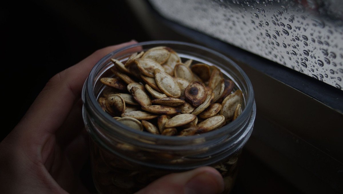 a photo of a hand holding a jar of roasted and salted pumpkin seeds with their shell
