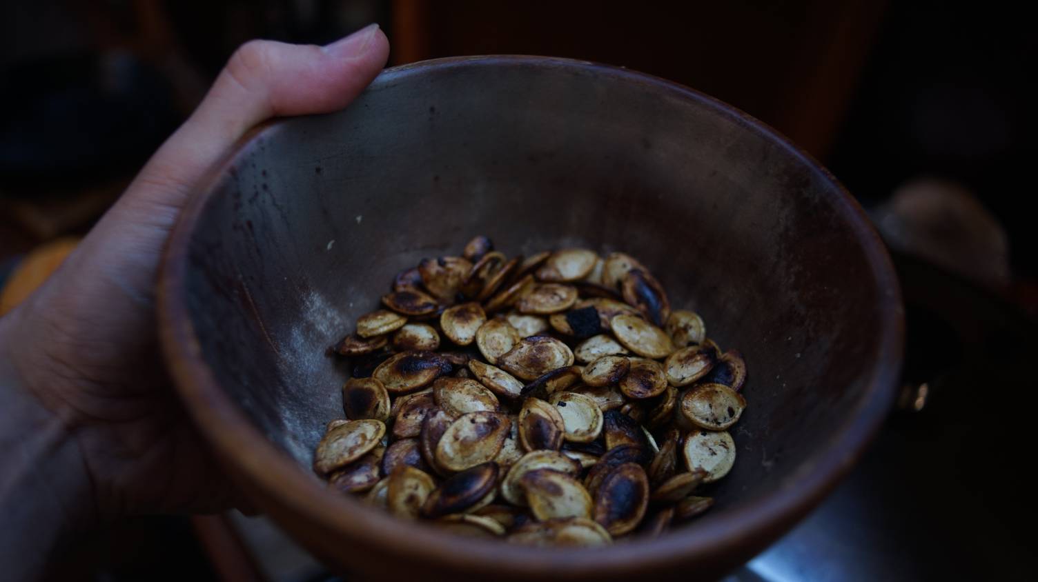 A photo of a hand holding a bowl of roasted pumpkin seeds