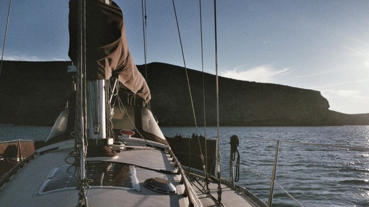 A photo from the perspective of someone standing on the bow of a sailboat, facing toward the back and showing water and hills in the background