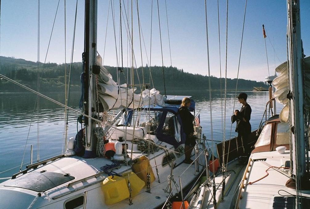Two sailboats rafted together in a quiet bay with a person on each boat standing and talking to each other