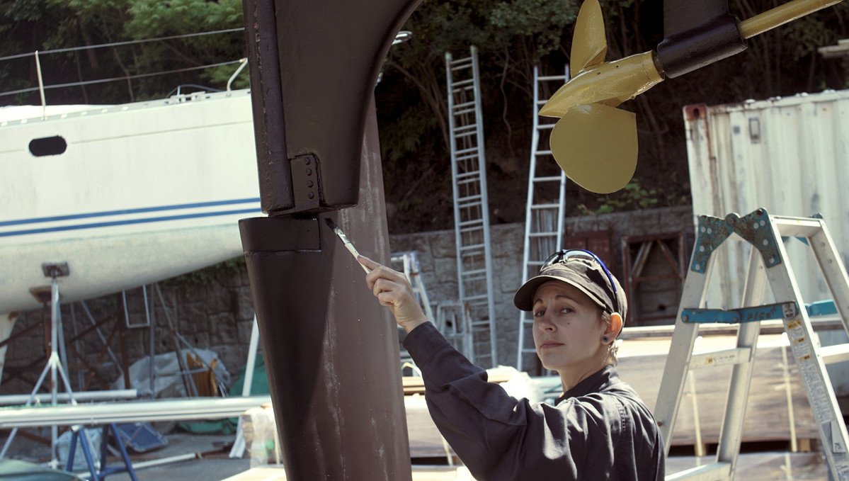 a photo of rek painting the rudder, with the shaft and prop painted in yellow in the background