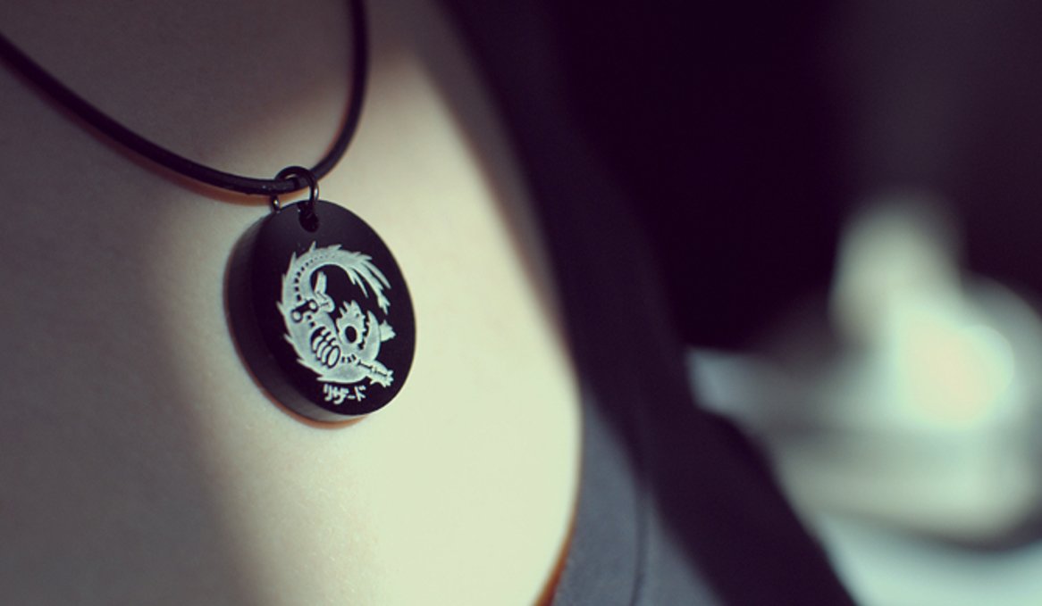 A photo of an acrylic pendant with the skeleton of a lizard creature etched into it