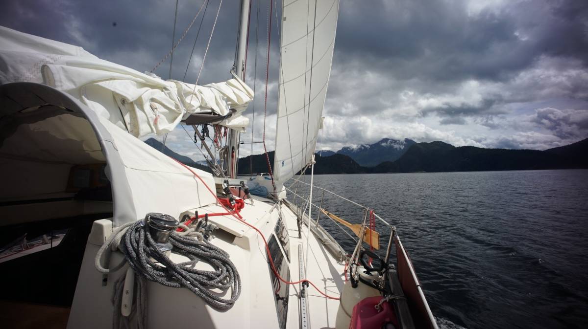 a sailboat sailing toward mountains on a grey day