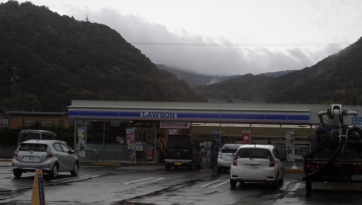 a photo of a small convenience store in rural japan, with fog and mountains in the background